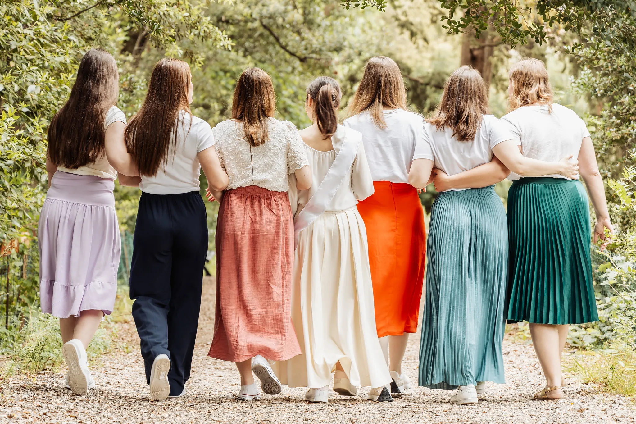 Groupe de filles de dos marchant bras dessus bras dessous dans un parc
