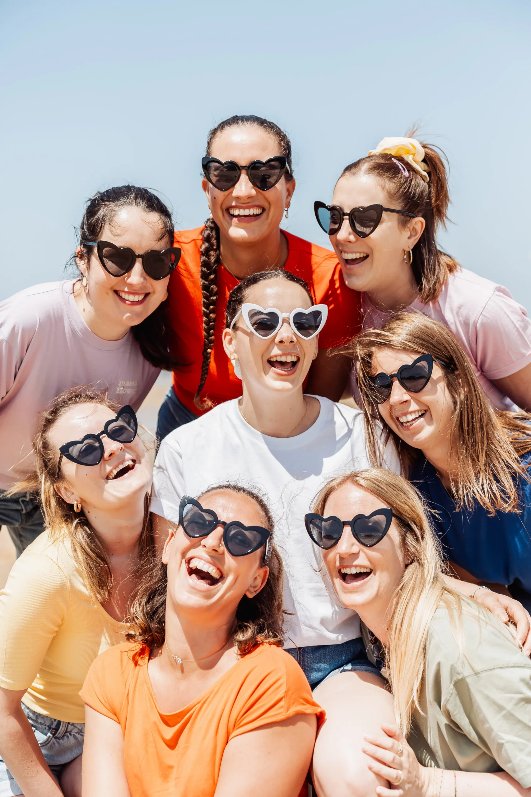 Portrait en contre-plongée de huit amies en lunettes cœur souriantes pendant un EVJF à Arcachon.