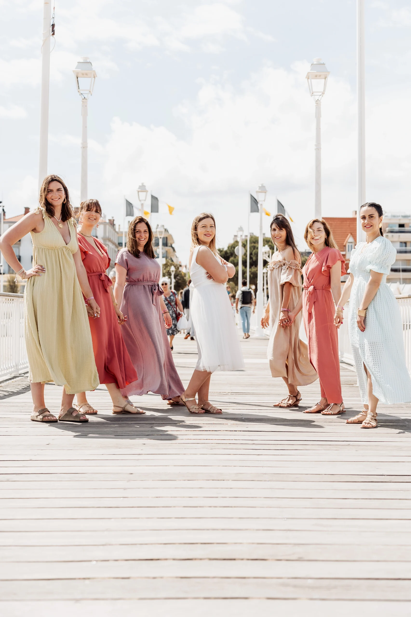 Photo de groupe EVJF à Arcachon avec la future mariée et ses amies en robes colorées sur la jetée.