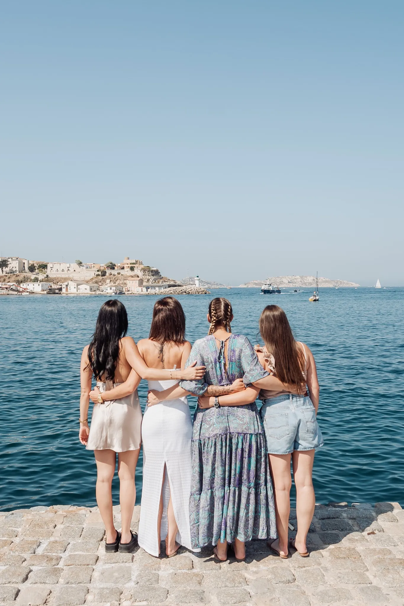 Photo EVJF à Marseille avec un petit groupe vu de dos face à la mer, bras enlacés et ambiance estivale
