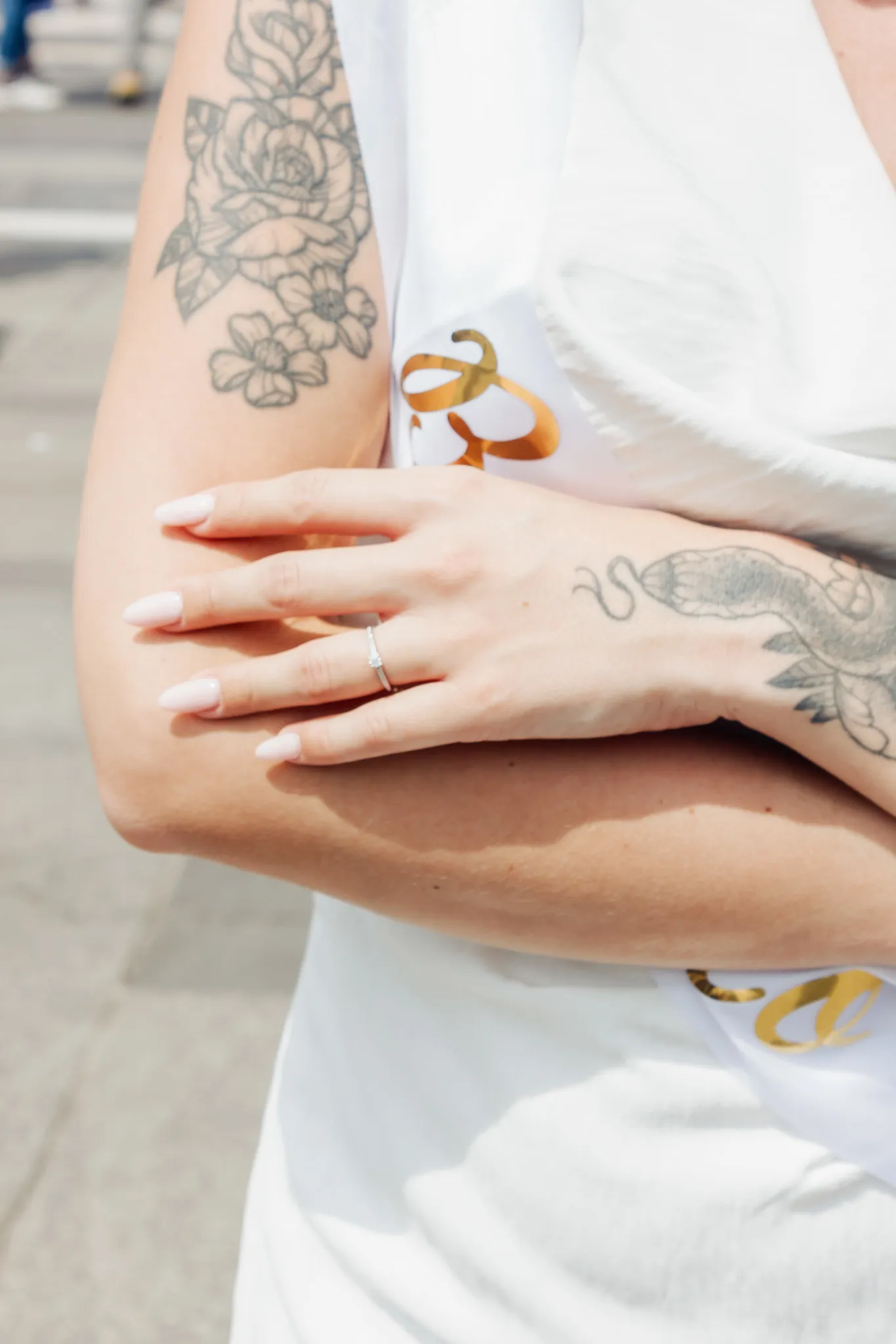 Gros plan sur la main d’une future mariée avec une bague de fiançailles, bras croisés, tatouages visibles, lors d’un EVJF à Milan.