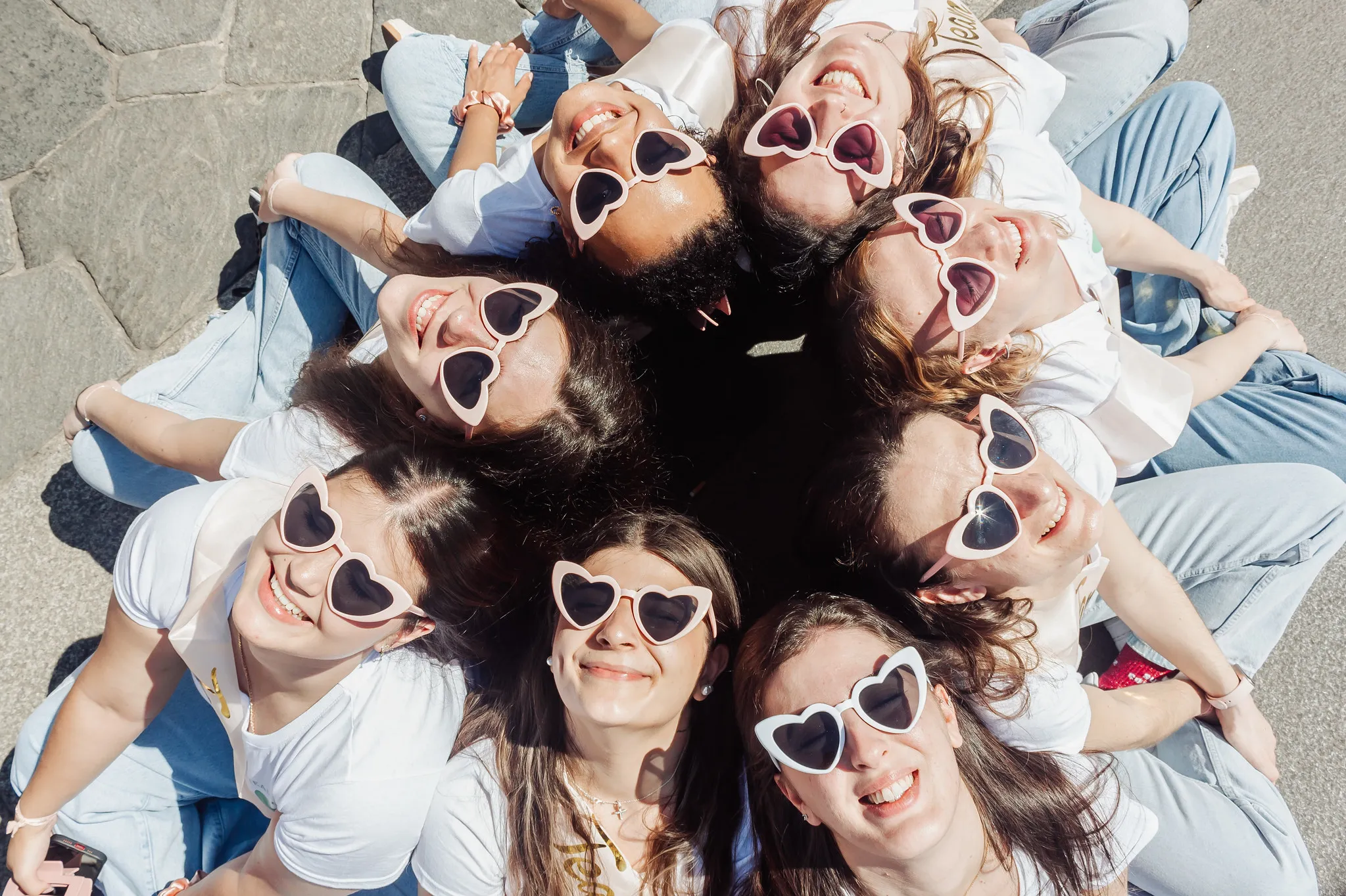 Groupe de femmes assises en cercle, toutes portant des lunettes en forme de cœur, souriantes et joyeuses pendant un EVJF à Milan.