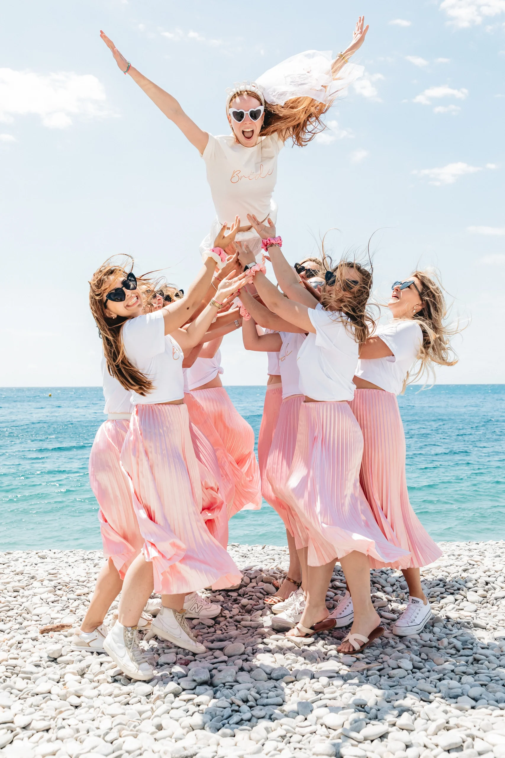 evjf-nice-saut-mariee EVJF à Nice – La future mariée s’envole dans les airs portée par ses amies en jupes roses face à la mer Méditerranée