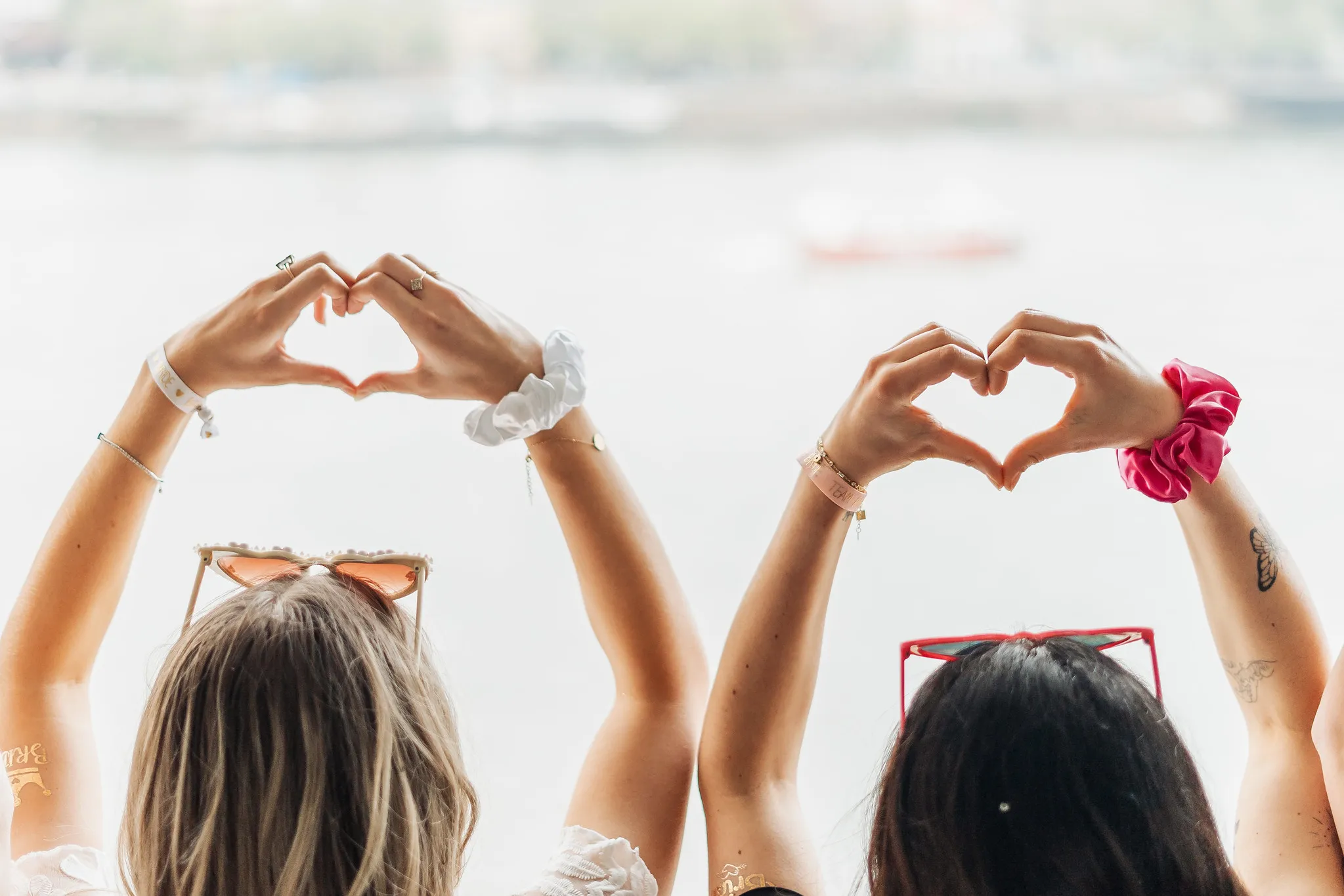 Deux femmes de dos levant les bras et formant un cœur avec leurs mains, face au fleuve Douro à Porto, lors d’un EVJF.