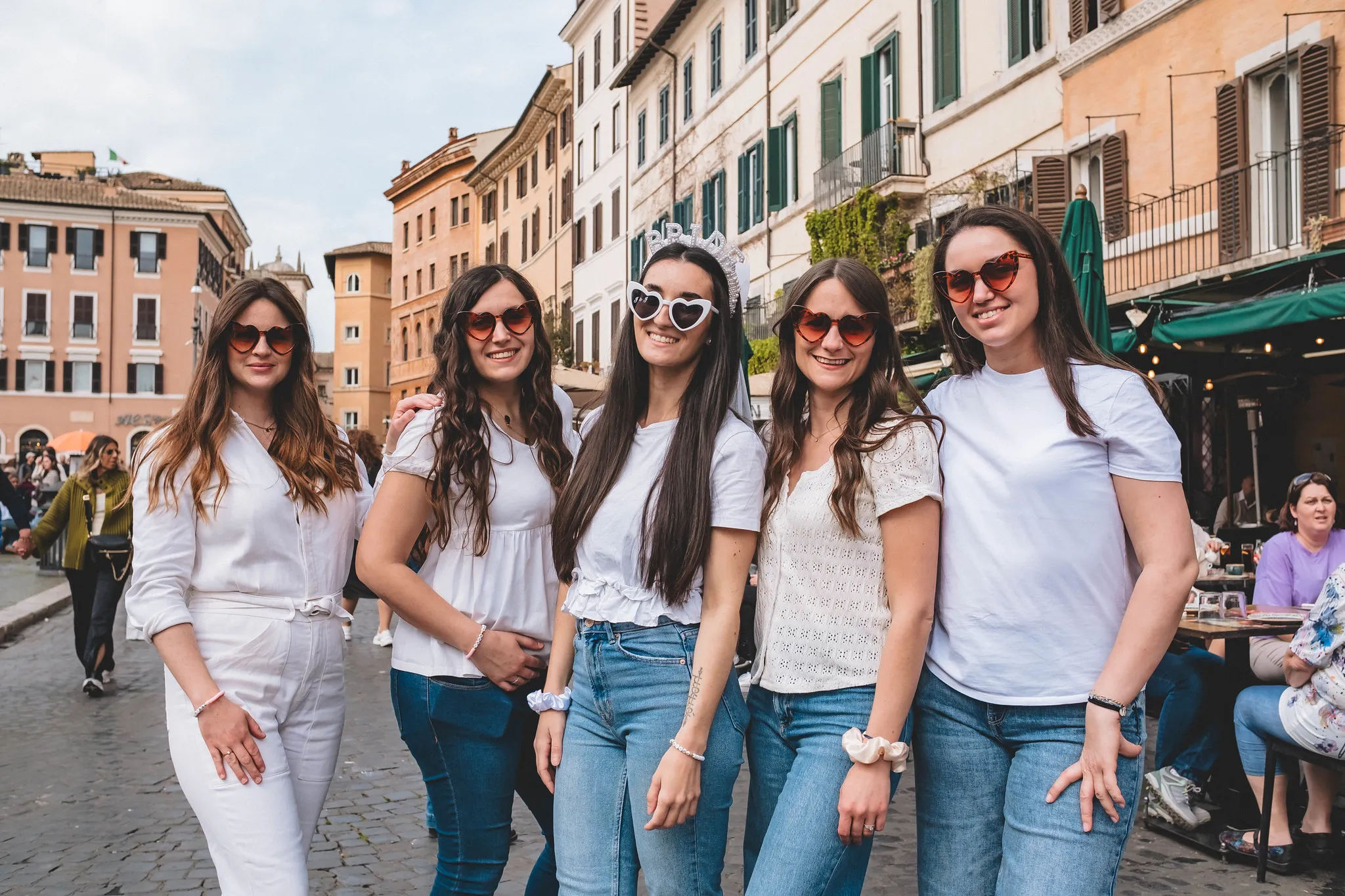 Cinq femmes souriantes vêtues de blanc et de jean posent ensemble dans les rues pittoresques de Rome pendant un EVJF.