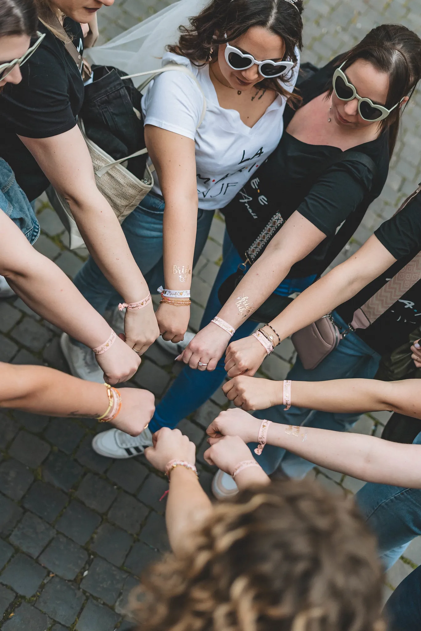 Gros plan sur un cercle de poings fermés portant des bracelets EVJF assortis, symbolisant l’unité du groupe lors d’un EVJF à Rome.