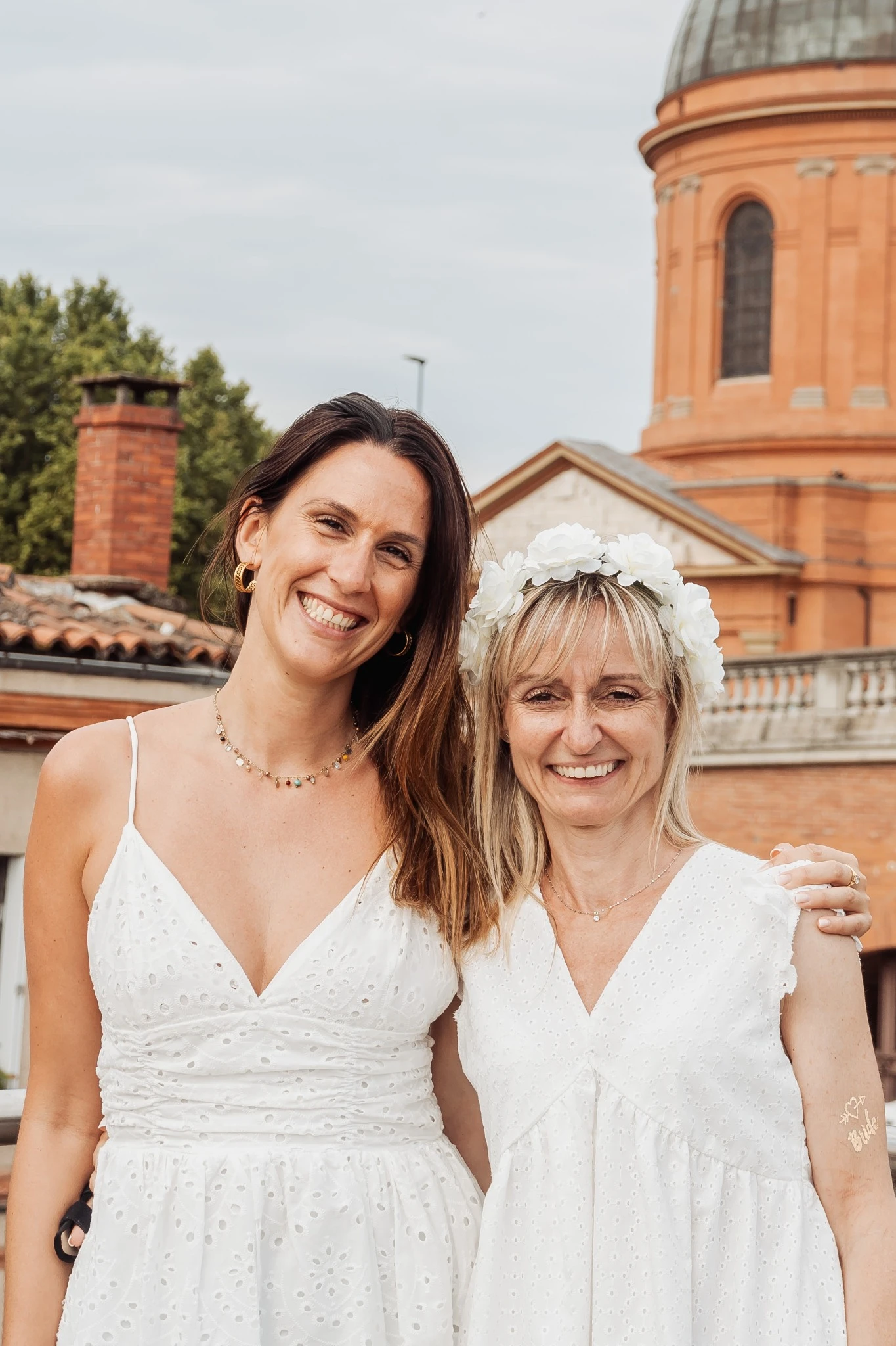 La future mariée et une amie posant ensemble devant un monument emblématique de Toulouse, toutes deux en robes blanches, souriantes.