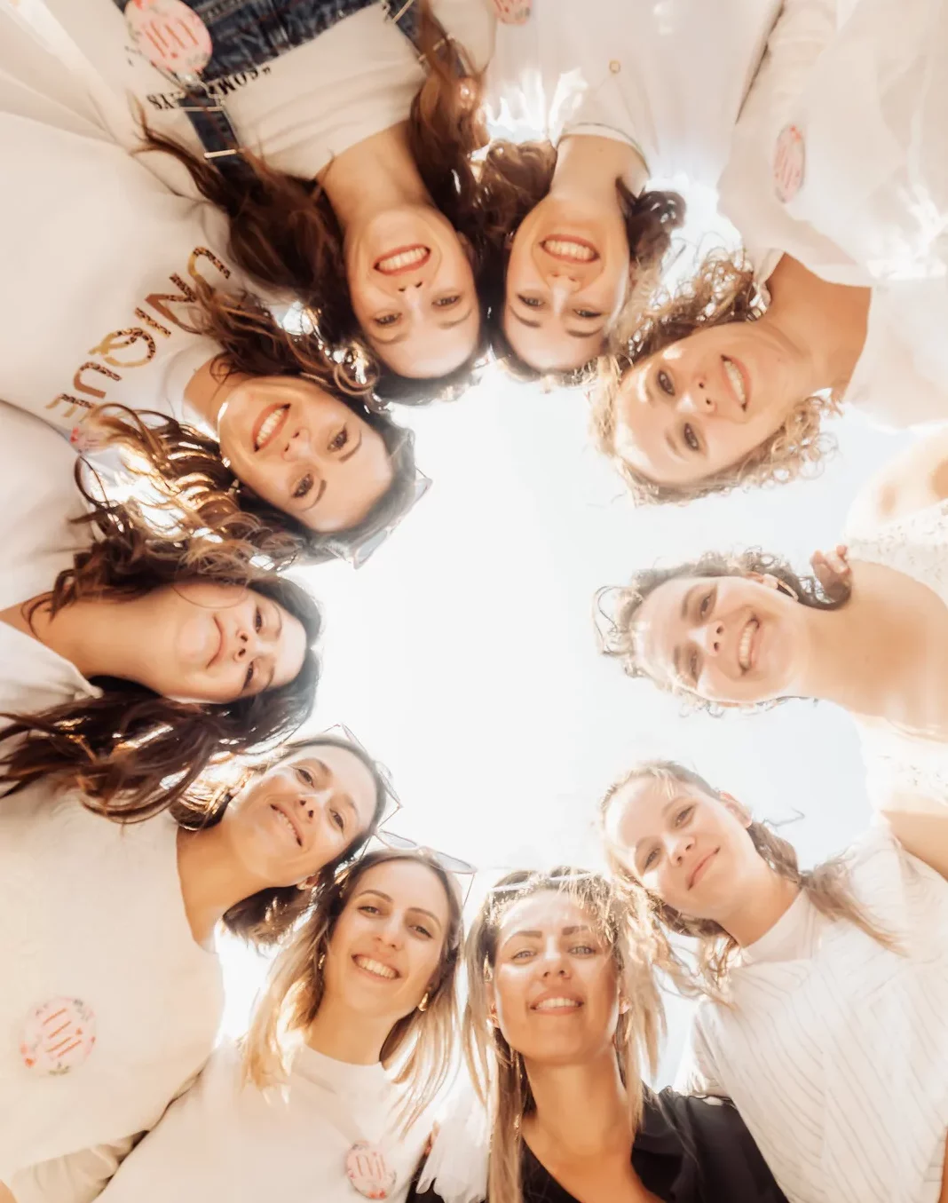 Photo d’un groupe de femmes réunies en cercle pour un EVJF à Marseille, souriantes et joyeuses sous un ciel bleu, prises en contre-plongée.