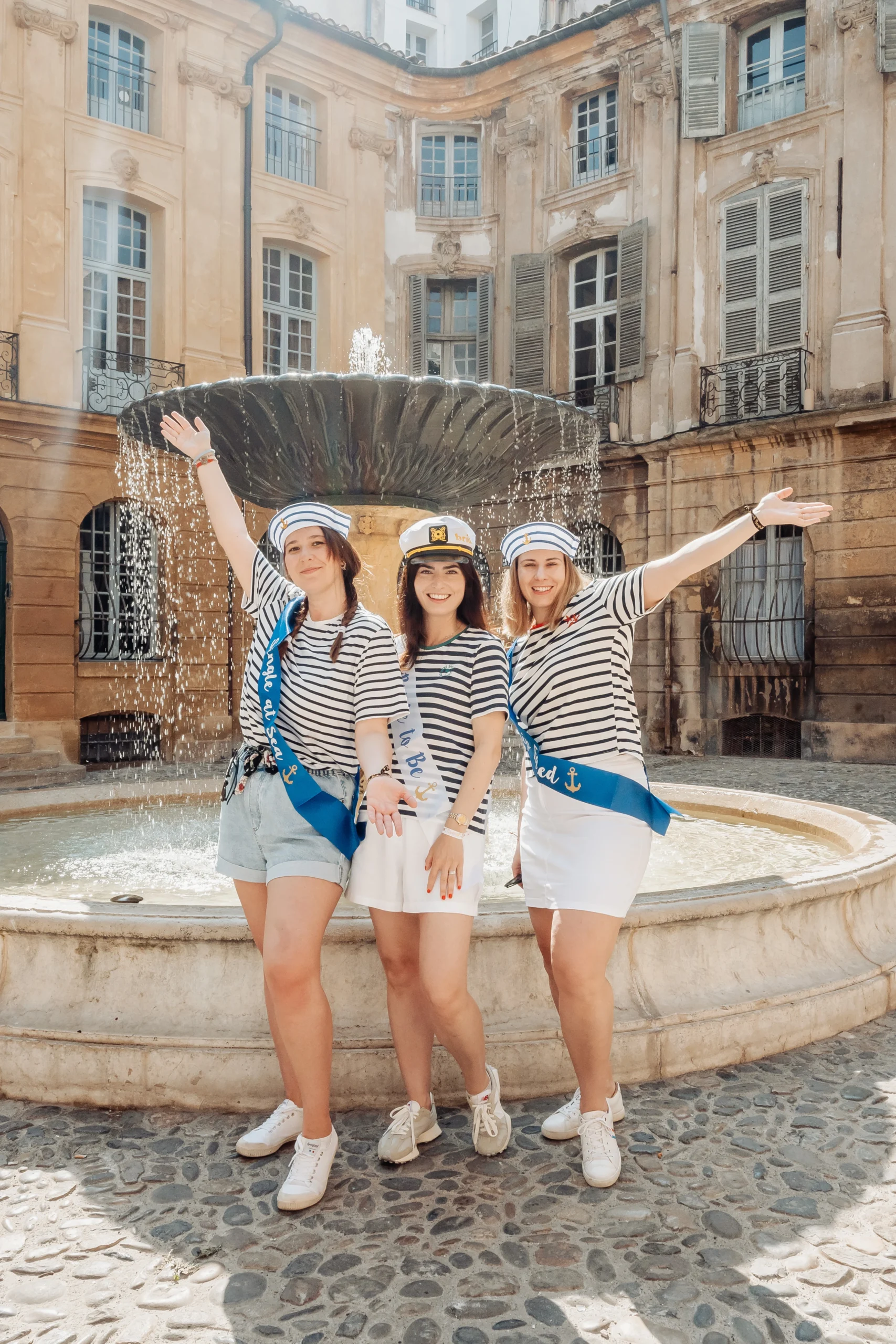 Photo EVJF à Aix-en-Provence devant une fontaine historique, avec des amies en marinière et chapeaux de marin, ambiance festive et ensoleillée